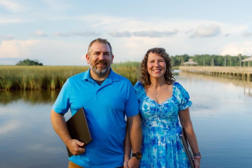 Anna and Bryan Cirlot, web designers and founders of Salt Marsh Digital, standing by a Gulf Coast marsh and boardwalk with laptops
